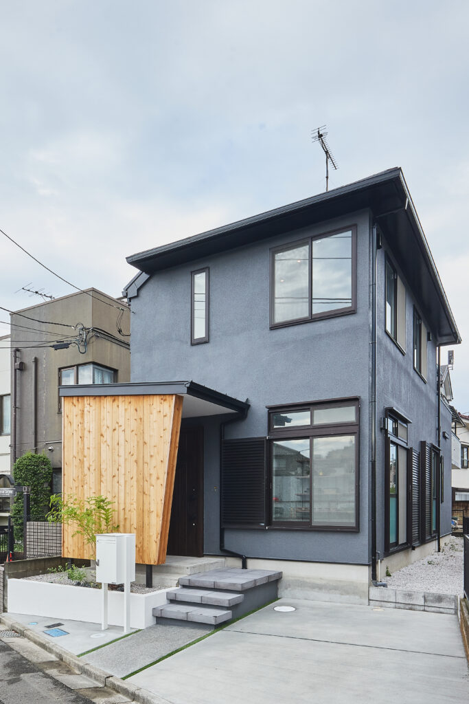 モルタル外壁をグレーに塗装し、玄関ポーチにアカシア無垢材を採用した戸建て外観。