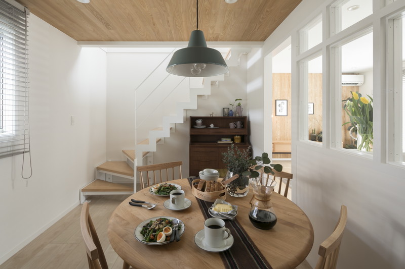 北欧スタイルのダイニングテーブルとペンダントライト。背後に造作のスケルトン階段が見える空間。