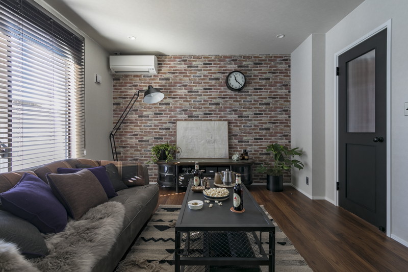 ヴィンテージ家具とレンガ調の壁紙を合わせたリビングルーム。黒い扉が空間を引き締めるリノベーション事例。